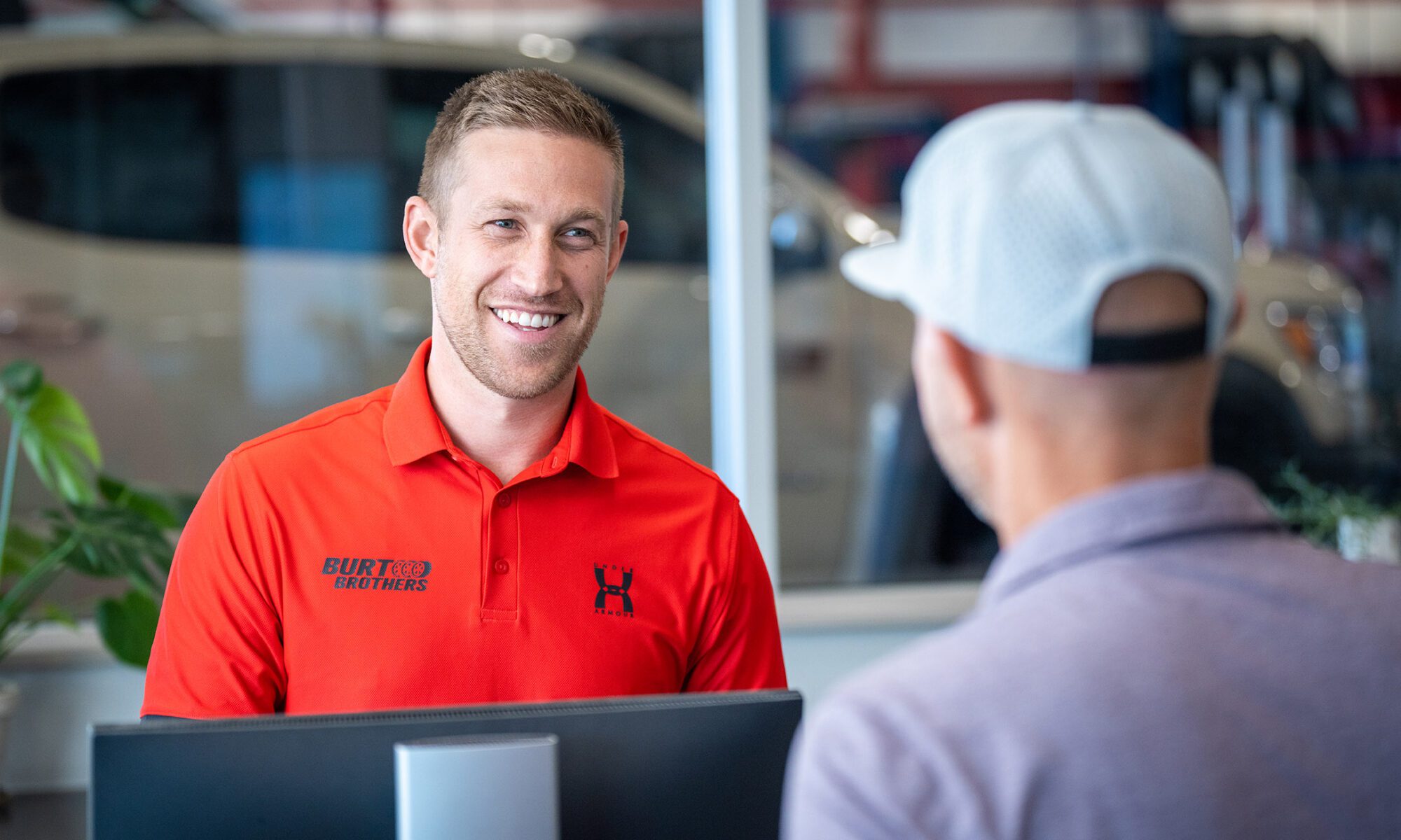 A smiling Burt Brothers dealership employee greets a customer seated across a counter.