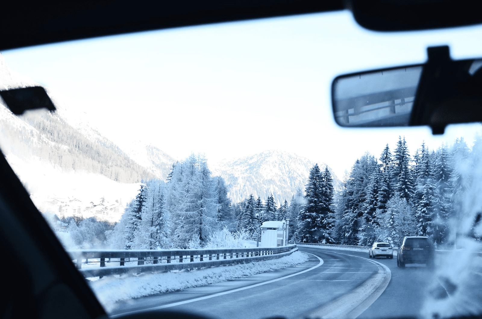 Dashboard view on a snowy winter road, with snow-covered trees lining the roadside