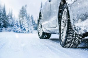 Close-up view of SUV with winter tires driving through snowy mountain roads with snow-covered trees.