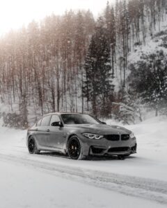 A sleek sedan with winter tires driving through a snowy forest.